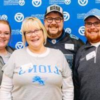 A family smiles for a photo in front of the GVSU backdrop